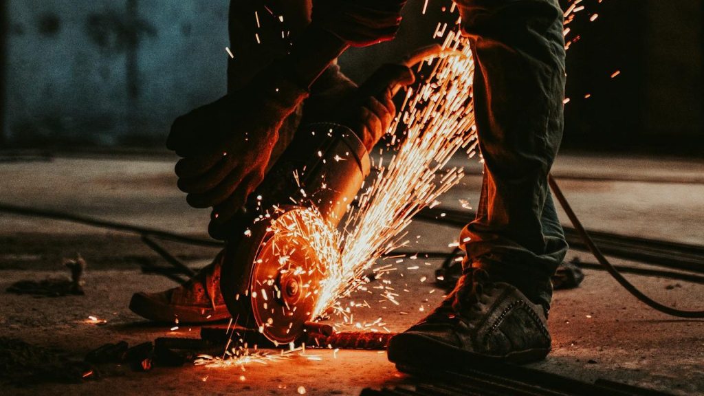 Worker in silhouette cutting metal with sparks in a construction site at sunset.